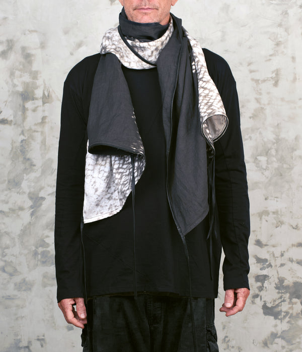 Person wearing a black outfit with a black & white tie dye patterned scarf against a textured gray background