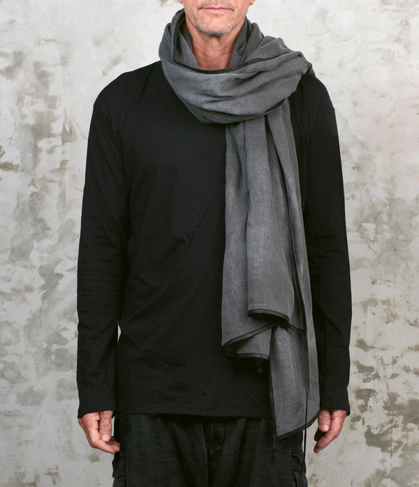 Person wearing a black outfit with a gray linen scarf against a textured wall.