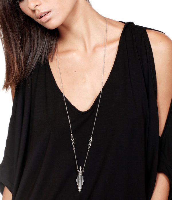 Person wearing a black top with a long necklace featuring a pendant.